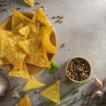 Pile of nachos, potato chips with spices lying in a wooden bowel. Concept of fast food background. Free place for text, top view.