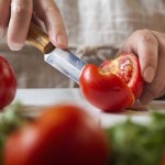 Chef slicing tomato using knife on the table in restaurant. Process of cutting and preparation food in kitchen.
