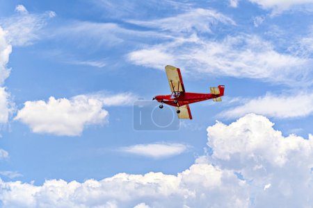 Red single-engine ultralight airplane flying in the blue sky with white clouds