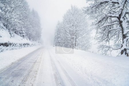 Foto de Mala visibilidad a lo largo de una carretera alpina cubierta de nieve durante una ventisca en invierno - Imagen libre de derechos