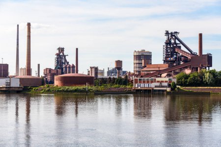 Foto de Vista de una planta de acero en la orilla de un río en un día de verano parcialmente nublado. Bremen, Alemania. - Imagen libre de derechos