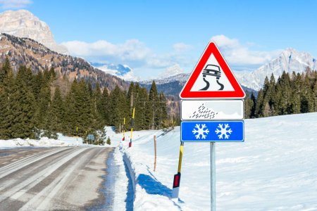 Foto de Señal de advertencia de carretera resbaladiza a lo largo de un camino de montaña en un día de invierno soleado - Imagen libre de derechos