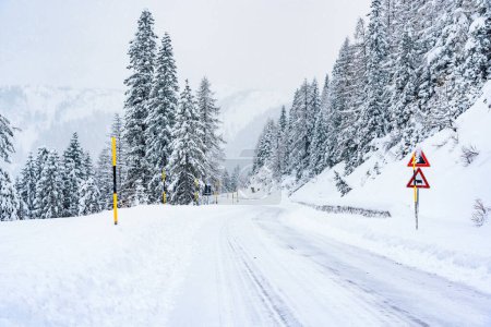 Foto de Camino de montaña sinuoso vacío cubierto de nieve durante una tormenta de nieve en invierno. Condiciones de conducción traicioneras. - Imagen libre de derechos