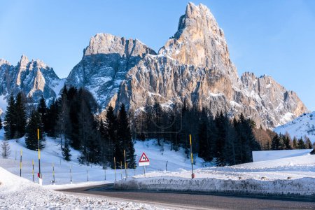 Foto de Winding mountain road running at the foot of a snowy rocky peak in the Alps on a clear winter day - Imagen libre de derechos