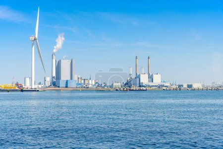 Foto de Centrales eléctricas de carbón con altas chimeneas en un puerto. Un aerogenerador alto está en primer plano. Rotterdam, Países Bajos. - Imagen libre de derechos