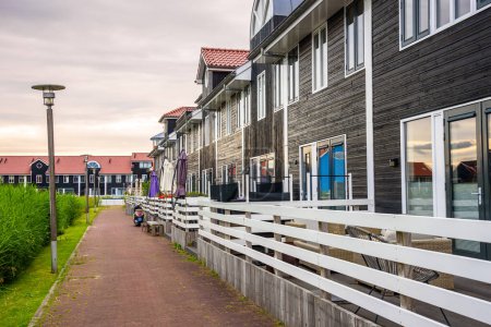 Foto de Nueva fila de casas de madera a lo largo de un sendero empedrado en un desarrollo de viviendas bajo el cielo nublado al atardecer. Groningen, Países Bajos. - Imagen libre de derechos