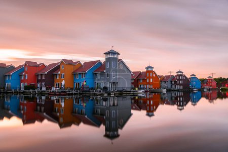 Téléchargez les photos : Maisons en rangée au bord du port multicolore au coucher du soleil. Longue exposition et réflexion dans l'eau. Groningen, Pays-Bas. - en image libre de droit