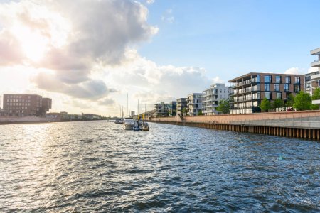 Photo for New apartment buildings in a redevelopped area along a former river harbour at sunset. Boats moored to a jetty are visible in the middle of the harbour. Bremen, Germany. - Royalty Free Image