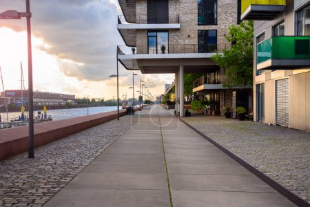 Téléchargez les photos : Harbourside footpath lined with modern apartment buildings at sunset in summer. Bremen, Germany. - en image libre de droit
