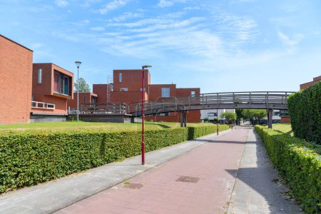 Foto de New brick houses along a deserted  bicycle path in a housing development. A wooded footbridge id in foreground. Zoetermeer, Netherlands. - Imagen libre de derechos
