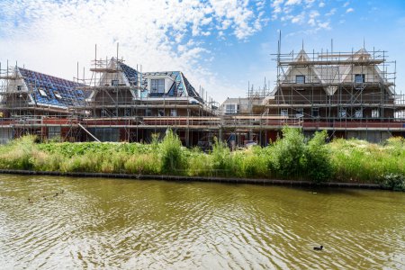 Foto de Houses under construction in a housing development along a canal in the countryside of Netherlands on a sunny summer day - Imagen libre de derechos