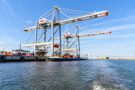 Photo for Cargo barge being loaded with containers while mooered to container terminal in a port on a sunny summer day. Rotterdam, Netherlands - Royalty Free Image