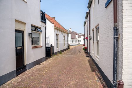 Narrow brick street lined with white holiday cottages in a seaside town on a sunny summer day. Katwijk aan Zee, Netherlands.