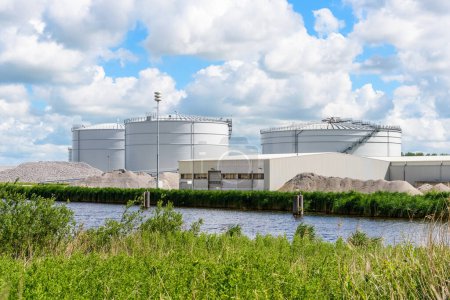 Téléchargez les photos : Grands digesteurs de biomasse dans une usine de biogaz le long d'un canal dans la campagne par une journée d'été ensoleillée. Groningen, Pays-Bas. - en image libre de droit