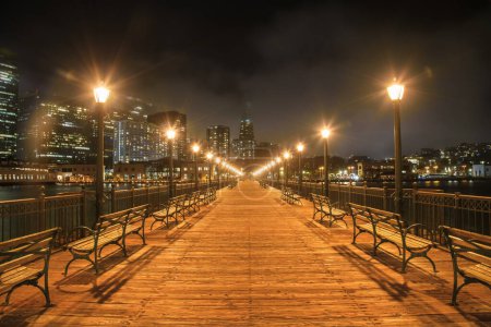 Téléchargez les photos : Quai sept en bois déserté bordé de lampadaires et de bancs à San Francisco la nuit. L'horizon du centre-ville partiellement couvert de brouillard est en arrière-plan. Californie, États-Unis. - en image libre de droit
