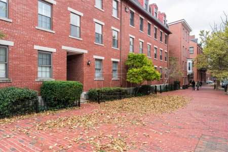 Foto de Edificios de apartamentos a lo largo de una acera de ladrillo cubierta de hojas en un día nublado de otoño.Charlestown, MA, USA. - Imagen libre de derechos
