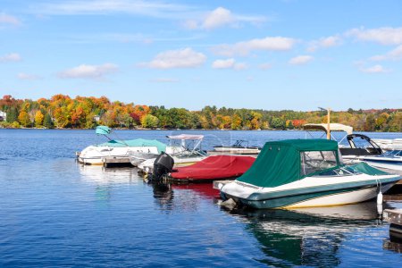 Foto de Barcos a motor atados a muelles de madera en un pequeño puerto en un lago rodeado de bosque en la cima de los colores otoñales. Huntsville, ON, Canadá. - Imagen libre de derechos