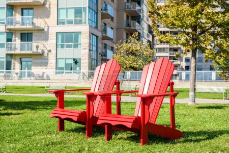 Photo for Red Adirondack chair on a grass in a park ona sunny autumn day. Apartment buildings are visible in background.Kingston, On, Canada. - Royalty Free Image