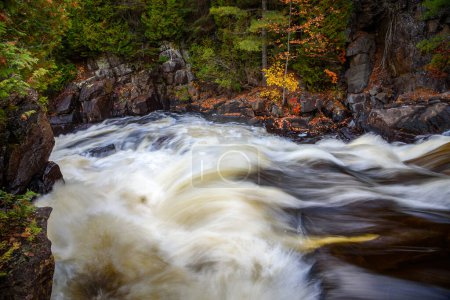 Foto de Agua que fluye rápidamente en la parte superior de una cascada a lo largo de un río que corre a través de un bosque en otoño. Ragged Falls park, ON, Canadá. - Imagen libre de derechos