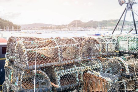Foto de Montón de ollas de cangrejo en un muelle en un puerto pesquero al atardecer. Conwy, Gales, Reino Unido. - Imagen libre de derechos