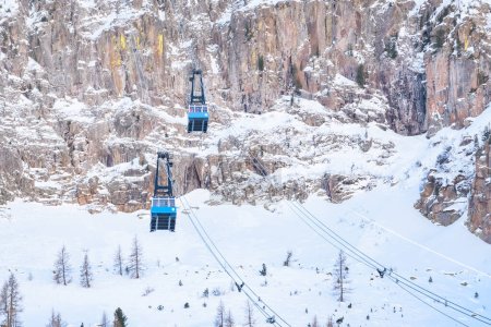 Foto de Vista de ángulo bajo de cabinas de teleférico transportando esquiadores y turistas arriba y abajo de un imponente pico rocoso nevado en invierno - Imagen libre de derechos
