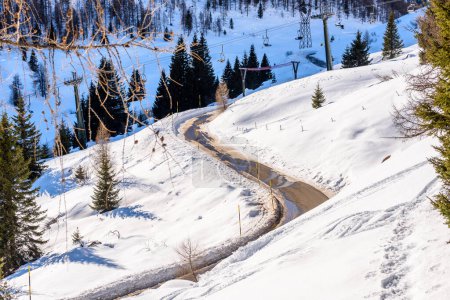 Foto de Camino helado vacío girando y subiendo una montaña nevada en un día soleado de invierno - Imagen libre de derechos
