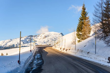 Foto de Desierto tramo de un camino de paso de montaña entre las laderas nevadas en un día de invierno soleado - Imagen libre de derechos