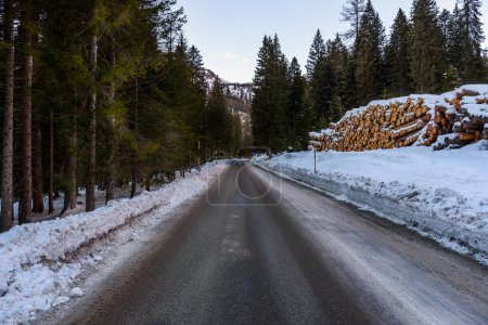 Téléchargez les photos : Route de montagne droite glacée à travers une forêt enneigée au crépuscule en hiver - en image libre de droit