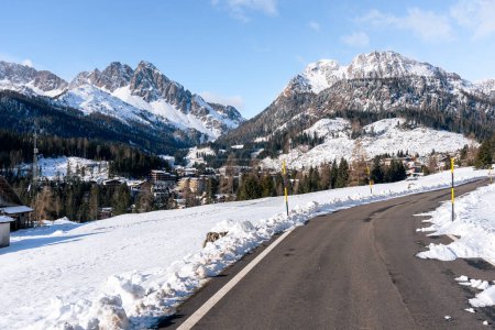 Téléchargez les photos : Route menant à un village de montagne entouré de montagnes imposantes couvertes de neige en hiver - en image libre de droit