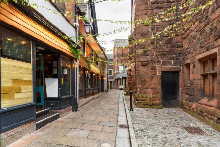 Photo for Deserted cobblestone alley lined with old stone buidings and restaurants in a historic central district. Chester, England, UK. - Royalty Free Image