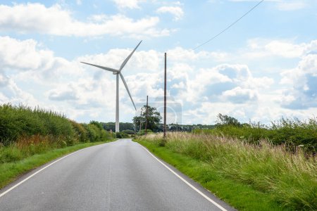 Foto de Turbina eólica a lo largo de una sinuosa carretera en Inglaterra en un día de verano parcialmente nublado. South Yorkshire, Inglaterra, Reino Unido - Imagen libre de derechos