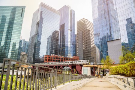 Deserted riverbank path in downtown Chicago with modern office towers in background. An elevated train is crossing the river on a double deck bridge. Illinois, USA.