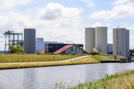 Photo for Factory with storage tanks and silos along a canal on partly cloudy summer day - Royalty Free Image