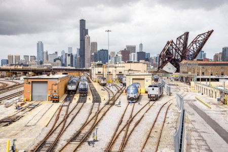 Diesellokomotiven in einem S-Bahn-Depot an einem bewölkten Tag. Die Skyline von Chicago und eine offene Zugbrücke sind im Hintergrund zu sehen. Illinois, USA.