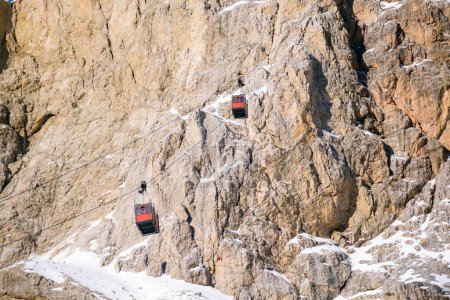 An einem sonnigen Wintertag befördern Gondelbahnen Touristen auf einem schneebedeckten Felsgipfel in den Alpen auf und ab. Dolomiten, Italien.