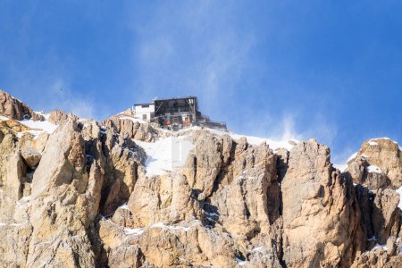 Blick auf eine Seilbahnstation auf einem schneebedeckten felsigen Berggipfel an einem windigen Wintertag. Dolomiten, Italien.