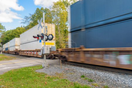 Foto de Tren de contenedores de movimiento rápido que pasa por un cruce de ferrocarril en una soleada mañana de otoño. Kingston, NY, Estados Unidos. - Imagen libre de derechos
