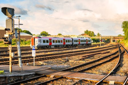Diesel-Personenzug verlässt im Sommer bei Sonnenuntergang einen Bahnhof. Zwei weitere Züge sind in der Ferne zu sehen. Chester, England, Großbritannien.