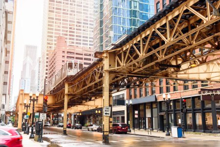 Blick auf einen Zug, der auf erhöhten Gleisen über eine Straße fährt, die von modernen Hochhäusern und traditionellen Backsteingebäuden in der Innenstadt Chicagos gesäumt ist. Illinois, USA.