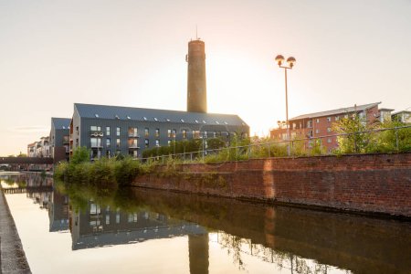 Téléchargez les photos : Immeubles modernes dans un réaménagement le long d'un canal sous le ciel clera au coucher du soleil en été. Chjester, Angleterre, Royaume-Uni. - en image libre de droit