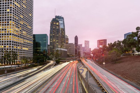 Photo for Long Exposure of a busy freeway bordering Los Angeles downtown high rise buildings at sunset in autumn. Light trails. CA, United States. - Royalty Free Image