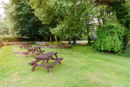 Foto de Mesas de picnic de madera vacías en la hierba en un parque en una soleada mañana de verano. Aston, Inglaterra, Reino Unido. - Imagen libre de derechos