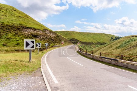Téléchargez les photos : Chevron panneaux routiers le long d'un virage serré le long d'une route sinueuse col de montagne en Angleterre par une journée d'été partiellement nuageux. Peak District National Park, Angleterre, Royaume-Uni. - en image libre de droit