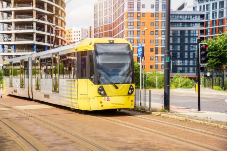 Foto de Tranvía amarillo en un tranvía que atraviesa un barrio residencial suburbano en un soleado día de verano. Un edificio de apartamentos en construcción está en segundo plano. Manchester, Inglaterra, Reino Unido. - Imagen libre de derechos