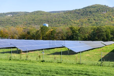 Planta de energía solar vallada con montañas boscosas de fondo en un día claro de otoño. Catskill Mountains, NY, Estados Unidos.