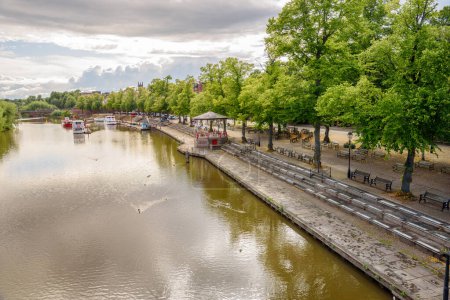 Téléchargez les photos : Vue d'en haut d'un parc riverain avec des bancs face à la rivière parmi les arbres et un kiosque à musique au coucher du soleil en été - en image libre de droit