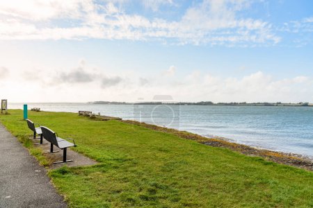Pequeño parque frente al mar con bancos en la hierba en el día claro de verano. Caernarfon, Gales, Reino Unido.