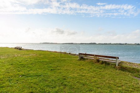 Foto de Empty woodend becnhed facing the sea in a small coastal park on a clear summer day. Caernarfon, Wales, UK. - Imagen libre de derechos