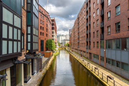Ziegelsteinerne Wohnhäuser an einem Kanal an einem sonnigen Sommertag. Ein steinerner Fußweg säumt den Kanal. Manchester, England, Großbritannien.