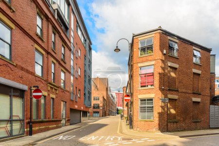 Foto de Calle adoquinada bordeada de edificios de ladrillo viejos convertidos en apartamentos y lofts y nuevo bloque de pisos en el distrito central en un día soleado de verano. Manchester, Inglaterra, Reino Unido. - Imagen libre de derechos